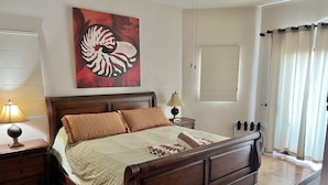A neatly made bed with a wooden headboard, a nightstand with a lamp, and a wall-mounted artwork.