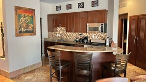 A kitchen with brown cabinets, a granite countertop, a microwave, a stove, and three bar stools.