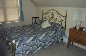 Un dormitorio con cama, mesita de noche, lámpara y ventana con cortinas.
