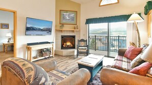 A cozy living room with a fireplace, comfortable seating, a television, and a scenic view through the window.