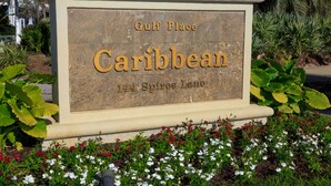 A sign for 'Caribbean' at 'Gulf Place, 144 Spires Lane' with a garden in front.