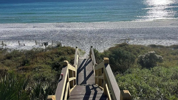 A wooden boardwalk leading to a beach with a clear view of the ocean.