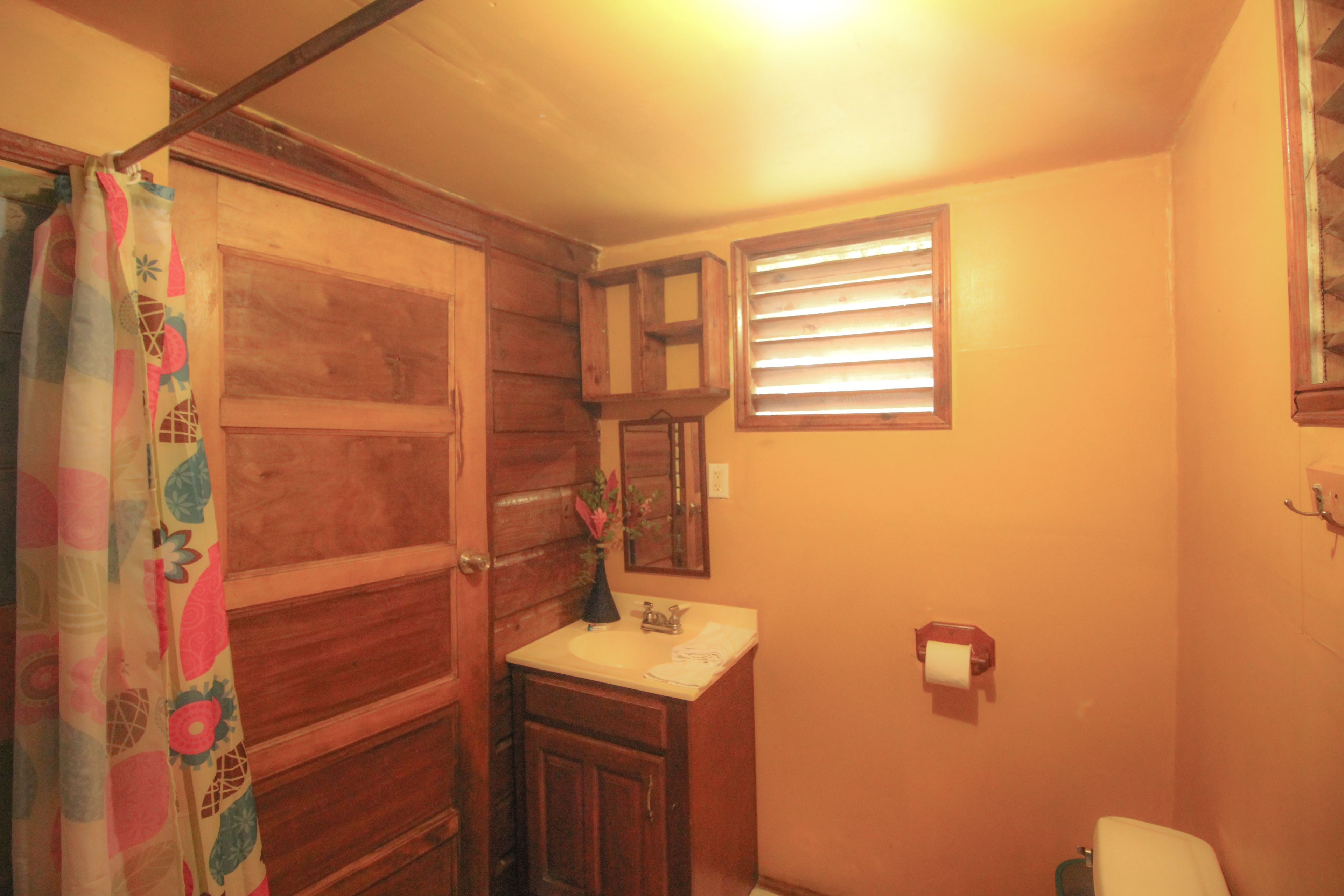 Une salle de bain avec des meubles en bois, un lavabo, un miroir et une fenêtre avec des stores.
