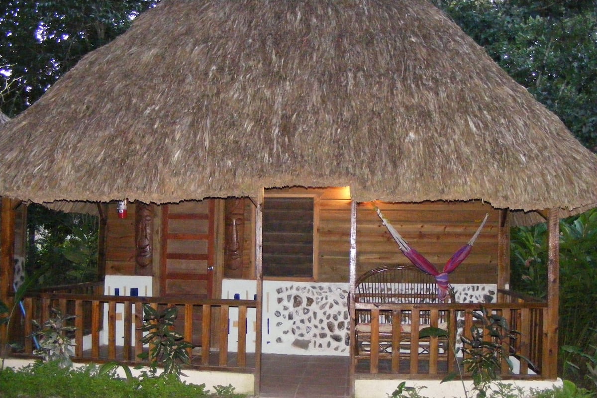 Una cabaña con techo de paja, un porche de madera y un muro de piedra.