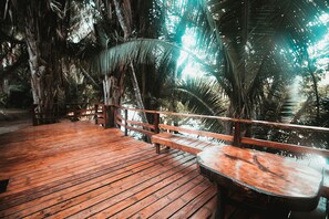 A wooden deck with benches and a table, surrounded by palm trees. - Cohune Palms River Cabanas (San Ignacio)