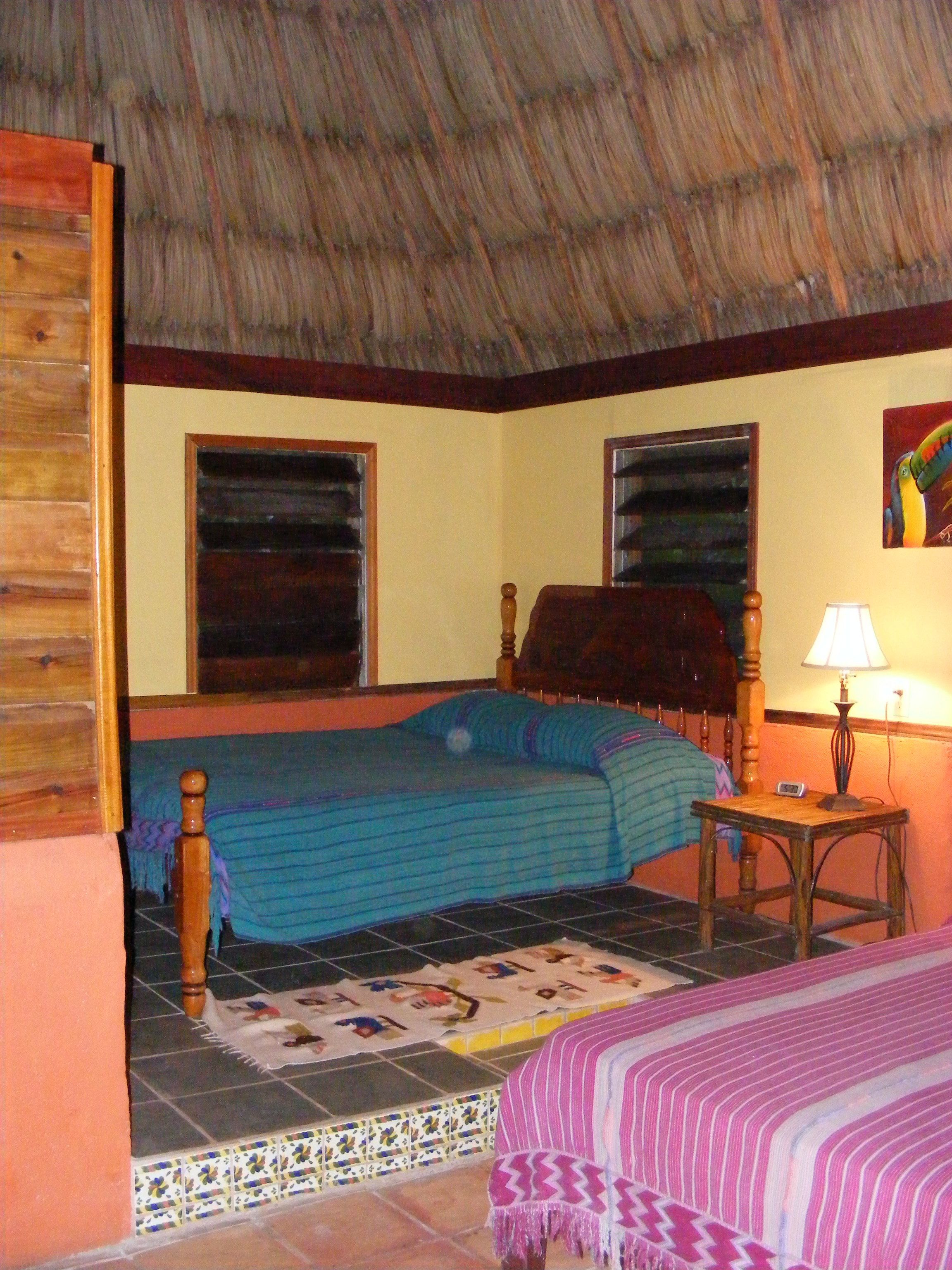 Una habitación con una cama, una mesita con una lámpara y una ventana.