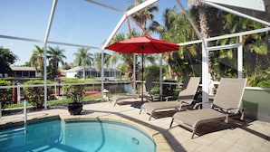 Un espace piscine avec des chaises longues et un parasol rouge.