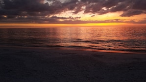 Une plage avec un coucher de soleil sur l’océan.