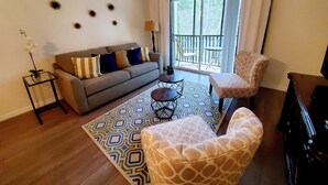 Un salon comprenant un canapé, un tapis à motifs, un fauteuil à l’effigie d’une girafe et une vue sur l’extérieur grâce à une porte coulissante.