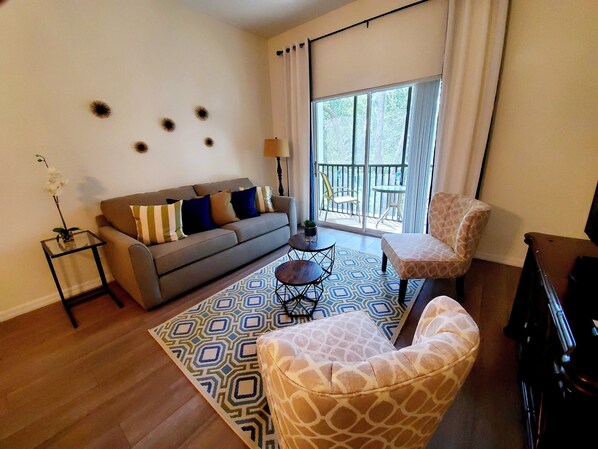 A living room with a sofa, a patterned rug, a giraffe-themed chair, and a view of the outdoors through a sliding door.