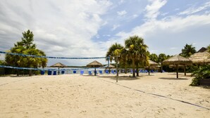 Un terrain de beach-volley avec un filet bleu, des palmiers et des structures à toits de chaume.