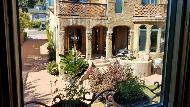 Une maison à deux étages dotée d’un balcon, d’une terrasse couverte et d’un jardin agrémenté de plantes en pot.