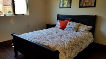 Un dormitorio con cama, mesita de noche, ventana y dos cuadros en la pared.