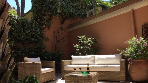 An outdoor seating area with wicker furniture, a table with a bottle and glasses, and potted plants. - Villa Borghese Oasis: Quiet, Large Apartment with WiFi, AC, Patio - Palm House 1 (Roma)