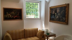 A room with a sofa, a chair, a small table, and two paintings on the walls. - Villa Borghese Oasis: Quiet, Large Apartment with WiFi, AC, Patio - Palm House 1 (Roma)