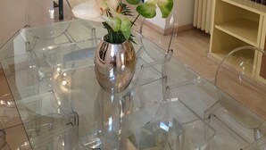 A dining area with a glass table, a vase with flowers, a white sofa, a bookshelf, and a painting on the wall. - Villa Borghese Oasis: Quiet, Large Apartment with WiFi, AC, Patio - Palm House 1 (Roma)