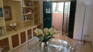 A dining area with a glass table and chairs, a bookshelf, and a green door leading outside. - Villa Borghese Oasis: Quiet, Large Apartment with WiFi, AC, Patio - Palm House 1 (Roma)