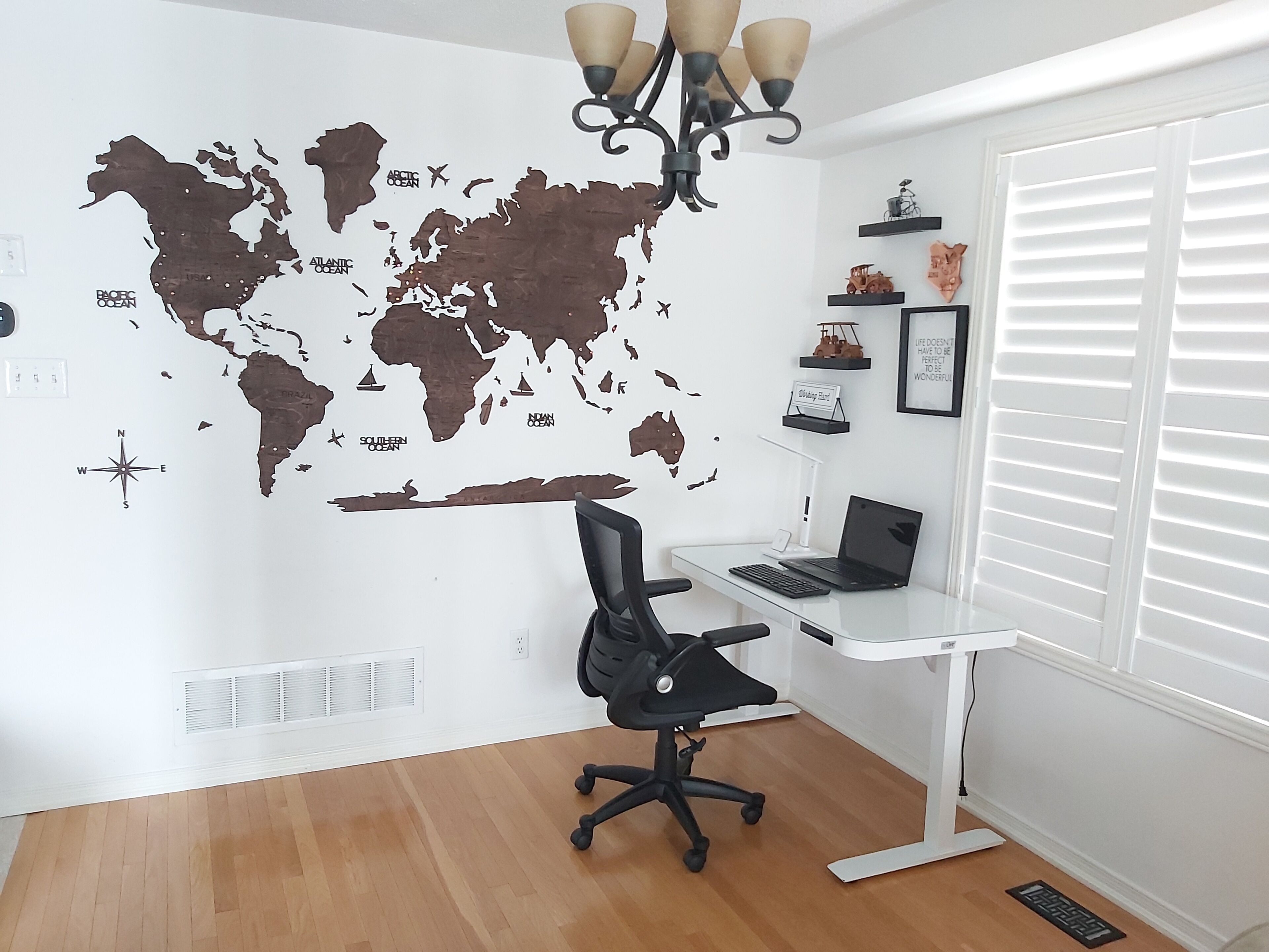 Una stanza con una mappa del mondo applicata al muro, una scrivania con un portatile, una sedia da ufficio nera e una finestra con persiane.