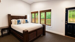 A bedroom with a wooden bed, a nightstand, a window with a view of greenery, and a dark door. - All Decked Out | Arcade Games | Amazing 5 BR |  Huge Deck | Fire Pit | Close to Everything WI Dells (Wisconsin Dells)
