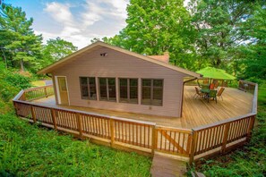 Escape to a serene cabin surrounded by lush greenery, featuring a spacious deck with a table and chairs.