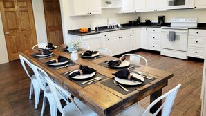 A dining area with a wooden table set for six, white chairs, white cabinets, a microwave, and a stove. - All Decked Out | Arcade Games | Amazing 5 BR |  Huge Deck | Fire Pit | Close to Everything WI Dells (Wisconsin Dells)