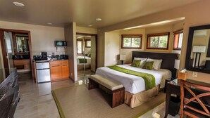 A hotel room with a bed, bedside table, desk, chair, kitchenette, and a bathroom with a mirror.