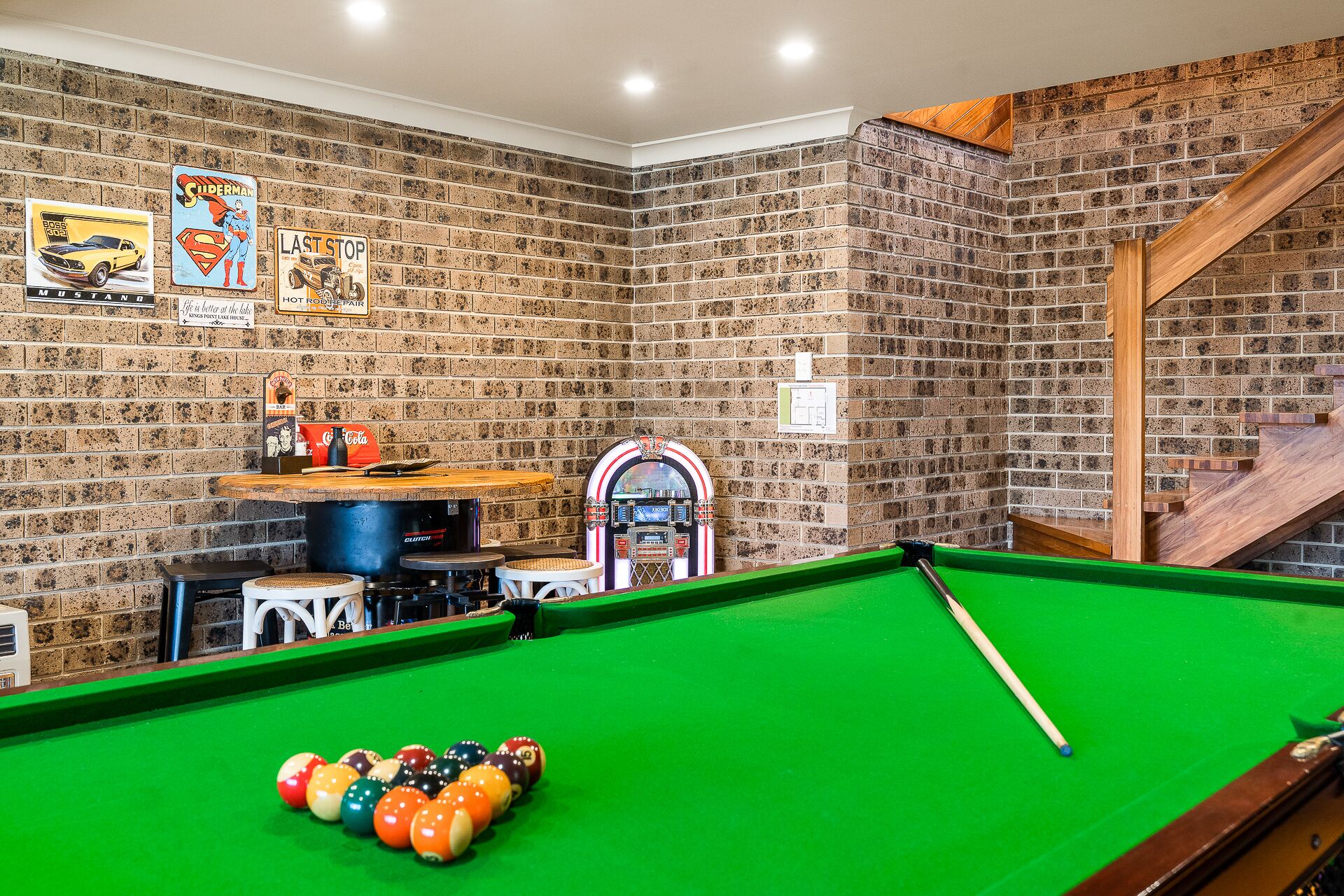 A pool table with a green felt surface, a pool cue, and colorful balls. There are arcade machines and a jukebox in the background.