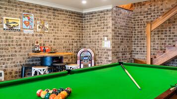 A pool table with a green felt surface, a pool cue, and colorful balls. There are arcade machines and a jukebox in the background.