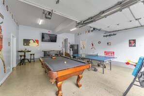 Una sala de billar con mesa de billar, mesa de ping pong y un televisor montado en la pared.