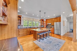 A spacious kitchen with wooden cabinets, a large island with bar stools, and a view of greenery outside.