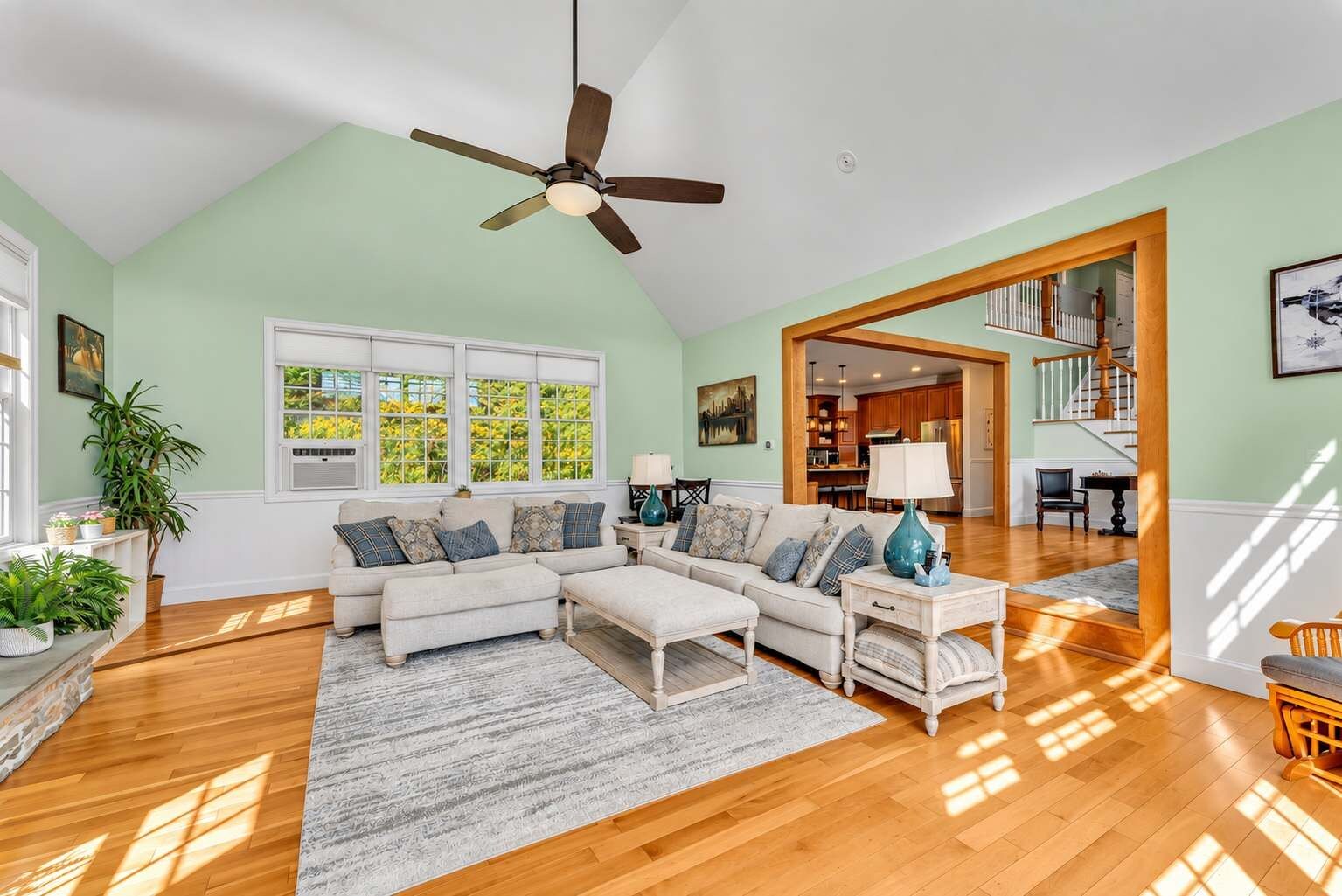 A spacious living room with a ceiling fan, a sofa set, a coffee table, and a view of the kitchen through an open doorway.