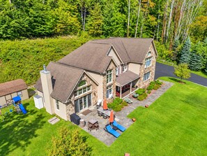 A two-story house with a stone facade, a covered patio with outdoor furniture, and a well-maintained lawn.