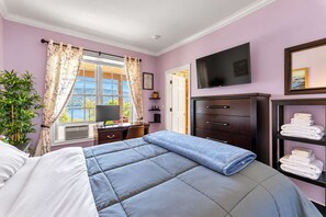 Una habitación de hotel con cama, escritorio, televisor, armario y estante con toallas.