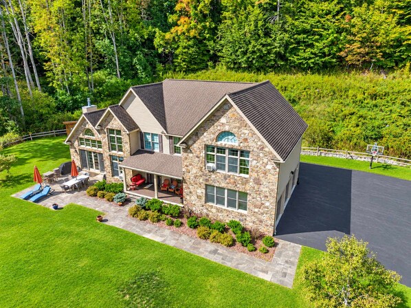 A two-story house with a stone facade, a covered patio, and a well-maintained lawn.