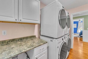 Un lavadero con lavadoras y secadoras de carga frontal apiladas, una encimera de granito y una puerta que da a otra habitación.