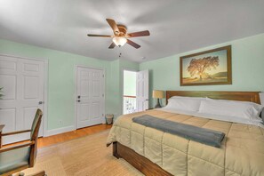 Une chambre à coucher avec un lit, un ventilateur de plafond, un tableau et une porte.