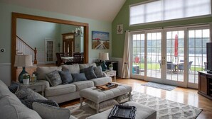 A spacious living room with a high ceiling, a large window, and a sliding glass door leading to an outdoor area. - Grand Slam - Lake House Cooperstown Dreams Park (Cooperstown)