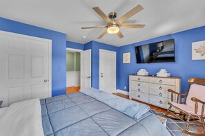 Une chambre à coucher comprenant un lit, une commode, un téléviseur et un ventilateur de plafond.
