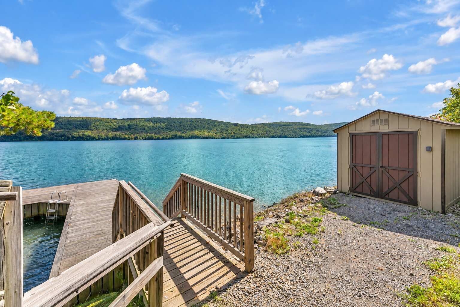 A wooden dock leading to a clear lake with a shed and a garage.