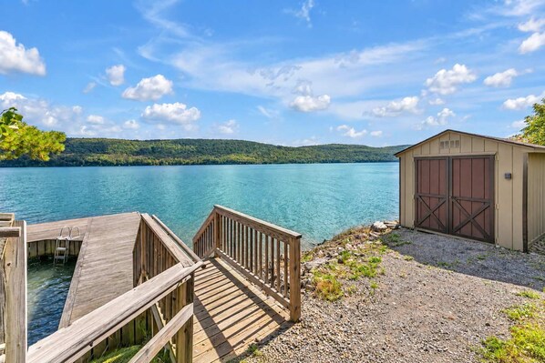 A wooden dock leading to a clear lake with a shed and a garage.