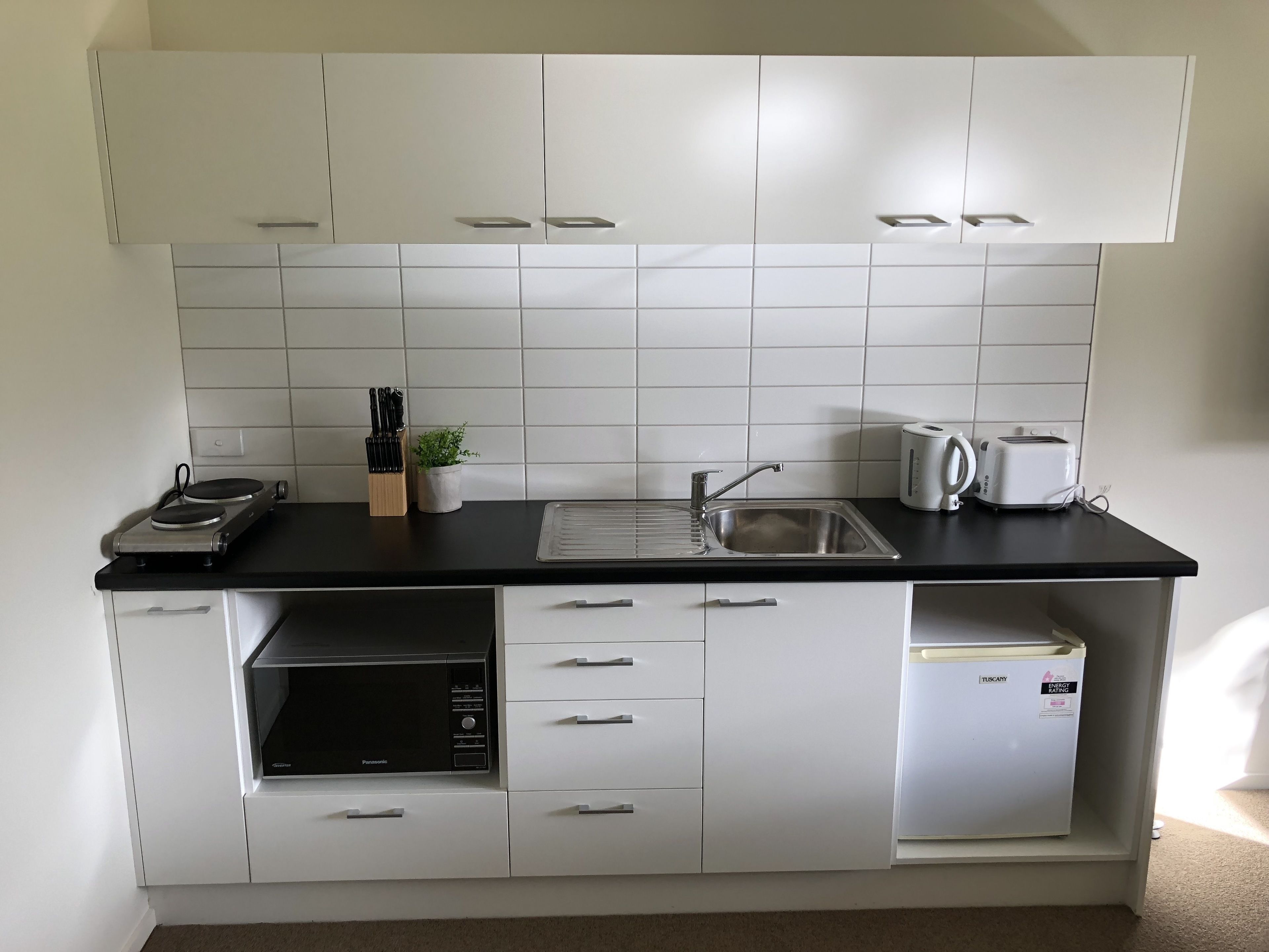 A compact kitchen with white cabinets, a black countertop, a sink, a toaster, and a microwave.