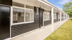 Filas de habitaciones de motel con puertas y ventanas correderas hacia el exterior, un pasillo cubierto y un área verde.