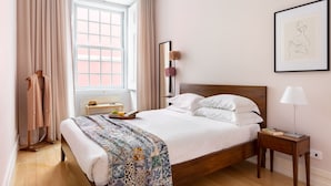 Un lit bien fait, recouvert d’une couvre-lit à motifs, une table de chevet avec une lampe et une fenêtre avec des rideaux.