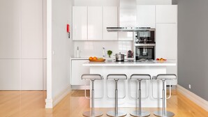 Une cuisine moderne avec des meubles blancs, une hotte en acier inoxydable, un four encastré et un coin bar avec des tabourets.