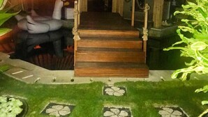 Un escalier en bois mène à un bâtiment au style rustique, entouré d’une végétation luxuriante et de plantes ornementales.