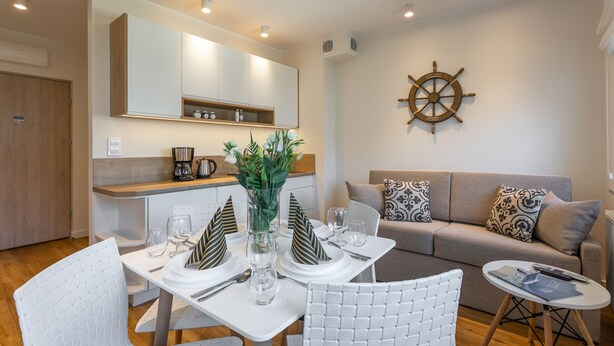 A modern kitchen with white cabinets, a coffee machine, and a dining area set with white chairs and a table. - Vacation apartment by the sea, vacation on the island of Usedom, Apartment VELA ROSA (Swinoujscie)