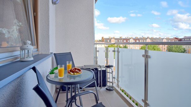 Ein Balkon mit Tisch, Stühlen, einer Laterne und einem Teller Essen.