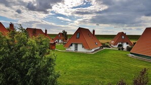Eine Gruppe traditioneller Häuser mit Satteldächern und Schornsteinen, umgeben von üppigen grünen Rasenflächen und Bäumen.