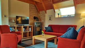 Ein gemütliches Wohnzimmer mit einem roten Sofa, einem Holztisch und einem Fernseher auf einem Holzständer.