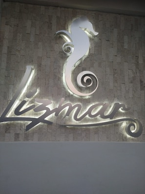 Paredes com uma placa metálica exibindo um 'L' e um 'Z' estilizados, com um design em espiral, indicando um hotel ou estabelecimento chamado 'Lizmar'.